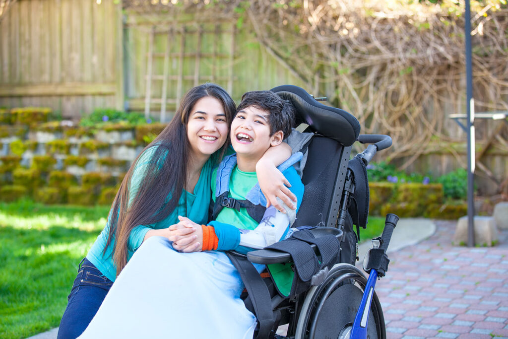 A woman and child in a wheelchair smiling for the camera.